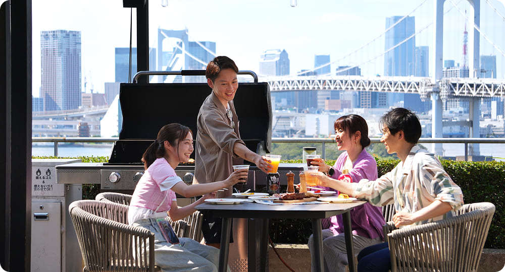 昼間のテラスでBBQをしながら笑顔で会話する若者たち