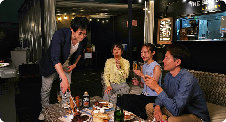 夜の屋外BBQで談笑しながら食事を楽しむ4人の男女